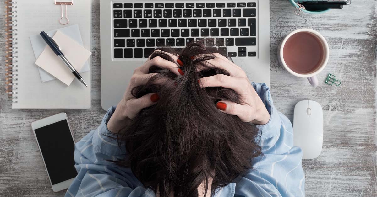 Person at a messy desk with their hands in their hair